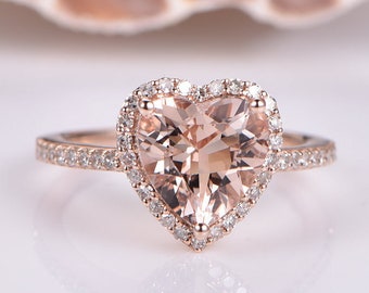May include: A rose gold engagement ring with a heart-shaped morganite center stone surrounded by a halo of smaller diamonds. The band is also set with diamonds.