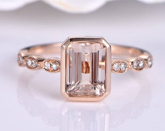 Könnte beinhalten: Ein Verlobungsring aus Roségold mit einem rechteckigen, klaren Edelstein, der in einer Zargenfassung sitzt. Die Band ist mit einer zarten Reihe kleiner, runder Diamanten verziert.