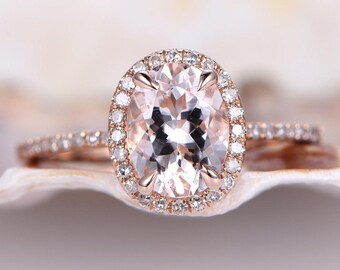 Op de afbeelding: Een verlovingsring van roségoud met een grote ovale morganiet in het midden, omringd door een halo van kleinere diamanten. De ring heeft ook een bijpassende band met kleinere diamanten.