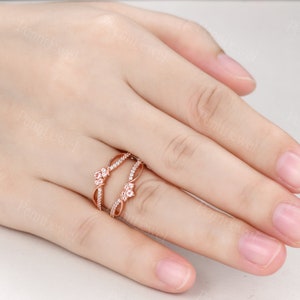 K&ouml;nnte beinhalten: Ein Ring aus Ros&eacute;gold mit zwei ineinander verschlungenen B&auml;ndern. Die B&auml;nder sind mit kleinen, klaren Steinen besetzt und haben ein florales Design.