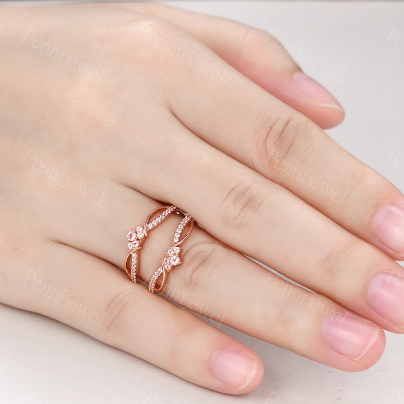 K&ouml;nnte beinhalten: Ein Ring aus Ros&eacute;gold mit zwei ineinander verschlungenen B&auml;ndern. Die B&auml;nder sind mit kleinen, klaren Steinen besetzt und haben ein florales Design.