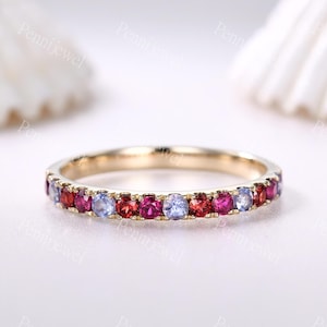May include: A delicate gold band ring with a row of alternating red and blue gemstones. The ring is set with small, round stones that create a colorful and elegant design.