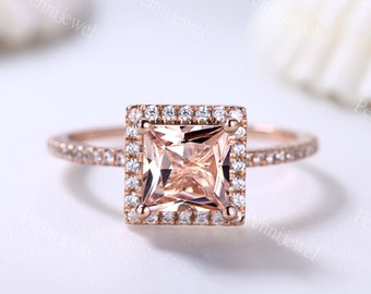 May include: A rose gold engagement ring with a square-shaped center stone and a halo of smaller stones. The band is also set with smaller stones.