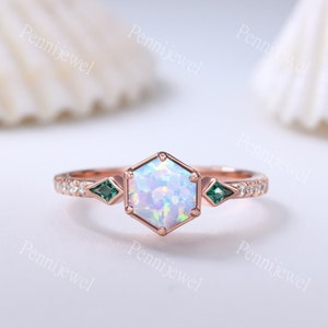 Könnte beinhalten: Ein Ring aus Roségold mit einem sechseckigen Opal-Edelstein und zwei smaragdgrünen Akzent-Steinen. Der Ring ist mit kleinen Diamanten um die Band herum besetzt.