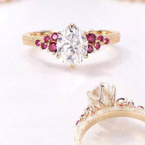 May include: A gold ring featuring a central oval-cut white gemstone flanked by clusters of small round-cut red rubies. The gold band displays an intricate engraved pattern along its surface, visible from both a top-down and a side profile view.
