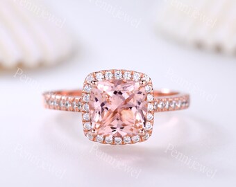 May include: A rose gold engagement ring with a square-shaped, light pink gemstone surrounded by a halo of smaller diamonds. The band is also set with smaller diamonds.