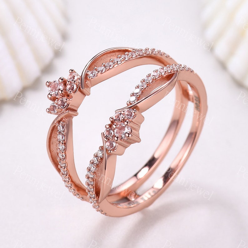 K&ouml;nnte beinhalten: Ros&eacute;goldring mit einem Doppelband-Design. Das Band ist mit kleinen, klaren Steinen besetzt und verf&uuml;gt &uuml;ber ein gr&ouml;&szlig;eres, blumenf&ouml;rmiges Design mit rosafarbenen Steinen.