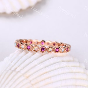 May include: A delicate eternity band ring with alternating pink and white gemstones. The ring is made of rose gold and features a scalloped edge.
