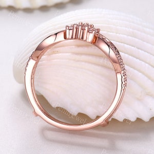 K&ouml;nnte beinhalten: Ein Ring aus Ros&eacute;gold mit einem zarten Design, das einen Cluster aus kleinen, klaren Steinen zeigt. Der Ring liegt auf einem wei&szlig;en Hintergrund.