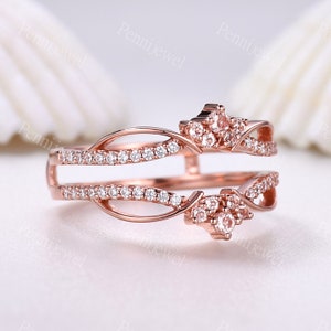 K&ouml;nnte beinhalten: Ein Ros&eacute;gold-Ring-Verst&auml;rker mit einem zarten, filigranen Design, das zwei B&auml;nder mit funkelnden Zirkonia-Steinen zeigt. Der Verst&auml;rker hat ein blattartiges Muster und ein kronenf&ouml;rmiges Design.