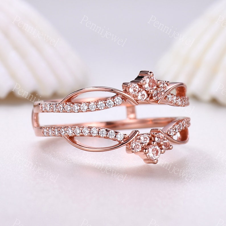 K&ouml;nnte beinhalten: Ein Ros&eacute;gold-Ring-Verst&auml;rker mit einem zarten, filigranen Design, das zwei B&auml;nder mit funkelnden Zirkonia-Steinen zeigt. Der Verst&auml;rker hat ein blattartiges Muster und ein kronenf&ouml;rmiges Design.