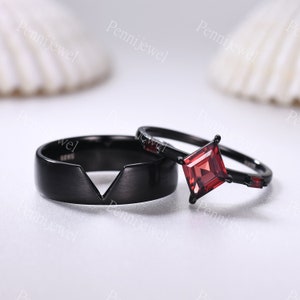 May include: A set of two black wedding bands. The band on the left has a V-shaped cutout. The band on the right has a square red gemstone.