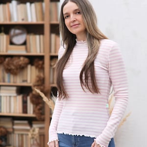 Może przedstawiać: Kobieta w długiej, różowo-białej, pasiastych koszulach z falbanką przy dekolcie. Koszula jest wykonana z miękkiej, lekkiej tkaniny.