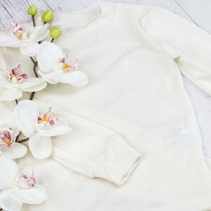 May include: A white long-sleeved shirt with a white orchid flower on top. The shirt is made of a soft, comfortable material.