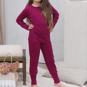 May include: A magenta-colored long-sleeved top and matching pants set. The top has a crew neck and the pants have a fitted ankle. The outfit is made of a soft, comfortable material. The set is suitable for sleepwear or loungewear.
