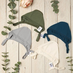 Peut inclure: Quatre bonnets pour bébé dans différentes couleurs : vert, gris, bleu et crème. Les bonnets sont faits d’un tissu doux et extensible et ont un nœud en haut.