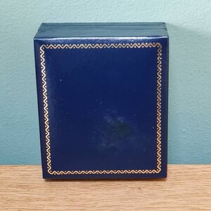 May include: A dark blue box with a gold decorative border. The box is made of a smooth, textured material.
