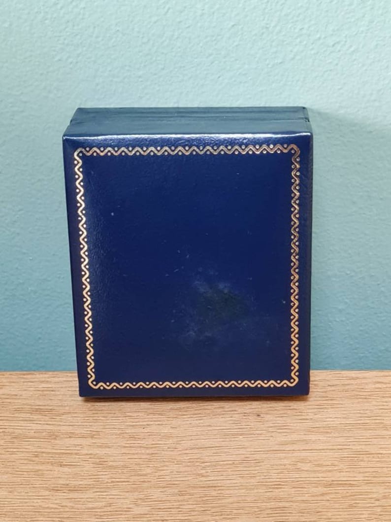 May include: A dark blue box with a gold decorative border. The box is made of a smooth, textured material.