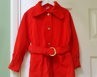 Puede incluir: Una chaqueta roja brillante con cuello, mangas largas y un cinturón dorado. La chaqueta tiene cierre de botones y dos bolsillos.