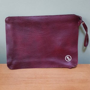 May include: A burgundy leather clutch with a white circle logo that says "RG" on it.