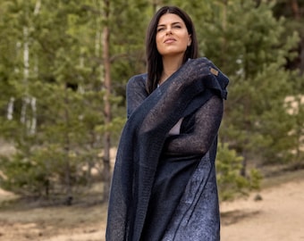 May include: A woman wearing a dark blue knitted shawl with a white dress. The shawl is draped over her shoulders and is made of a soft, lightweight material.