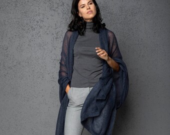May include: A woman wearing a dark blue knitted scarf over a gray turtleneck sweater and gray pants. The scarf is draped over her shoulders and hangs down to her knees.