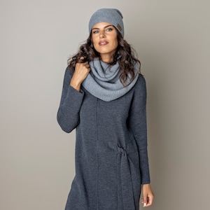 以下が含まれることがあります： グレーのニットドレスに、グレーのニットのインフィニティスカーフとビーニーを合わせた女性