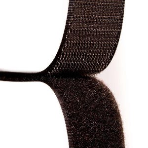 May include: Close-up of black hook and loop fastener tape. The tape is made of a soft, fuzzy material on one side and a rough, textured material on the other side.