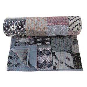 May include: A grey and black patchwork quilt with a floral pattern. The quilt is rolled up and has a blue border.