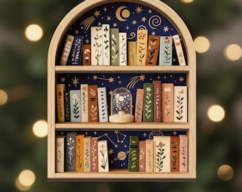 May include: Wooden bookshelf ornament with a celestial theme. The ornament features a wooden frame with three shelves filled with miniature books. The background is dark blue with stars, a crescent moon, and planets. A small glass globe sits on the middle shelf.