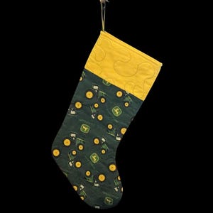 May include: A green and yellow Christmas stocking with a pattern of tractors. The stocking is quilted and has a yellow cuff.