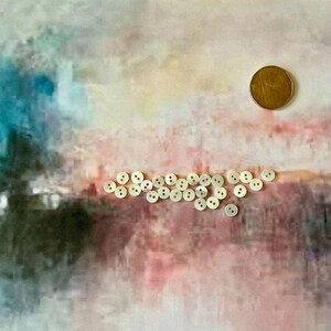 May include: A collection of small, round, off-white buttons with two holes, scattered on a colorful background. A gold-colored coin is also present. The buttons are likely for sewing or crafts.