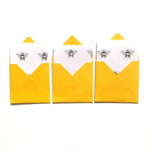May include: Three yellow envelopes with white paper inside. The paper has a repeating pattern of black bees.