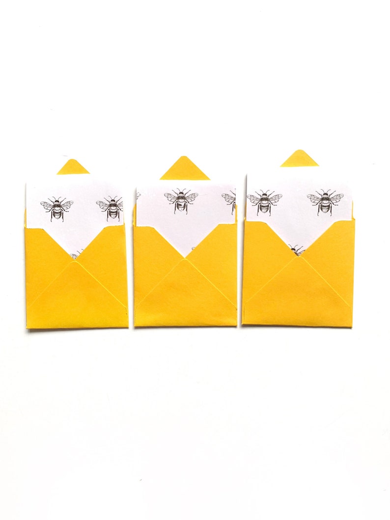 May include: Three yellow envelopes with white paper inside. The paper has a repeating pattern of black bees.