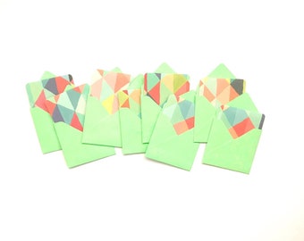 May include: A group of ten green envelopes with colorful geometric patterns inside. The envelopes are arranged in a row on a white background.