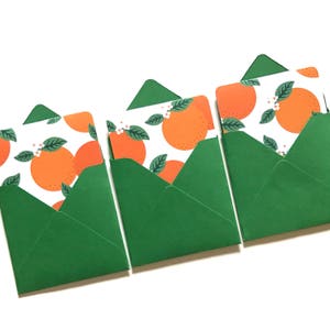 Pode incluir: Três envelopes verdes com inserções de papel branco com um padrão de fatias de laranja e flores brancas.
