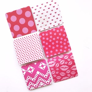 Può includere: Sei carte quadrate rosa e bianche con diversi disegni. I disegni includono pois, cuori, stelle, labbra e forme geometriche.