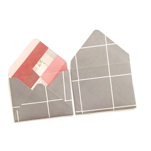May include: Two gray envelopes with a white grid pattern. One envelope is open and has a pink and red patterned paper inside.