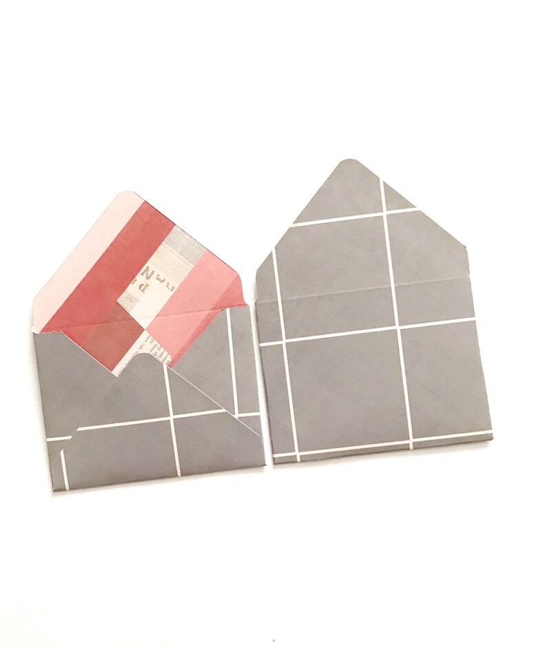 May include: Two gray envelopes with a white grid pattern. One envelope is open and has a pink and red patterned paper inside.