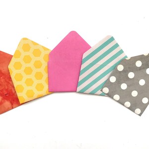 May include: Five small paper envelopes with different patterns. The envelopes are arranged in a semi-circle, with the pink envelope at the top and the gray envelope at the bottom. The patterns include honeycomb, stripes, polka dots, and a watercolor-like design.