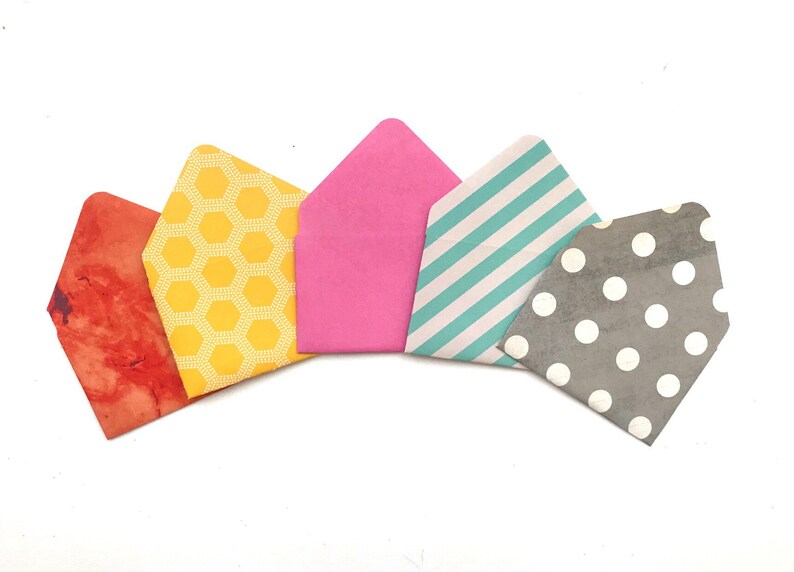 May include: Five small paper envelopes with different patterns. The envelopes are arranged in a semi-circle, with the pink envelope at the top and the gray envelope at the bottom. The patterns include honeycomb, stripes, polka dots, and a watercolor-like design.
