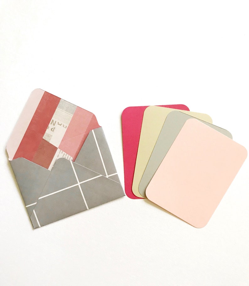 May include: A gray envelope with a white grid pattern and a pink and red striped flap. The envelope is open and a piece of paper with text is visible inside. There are five blank cards in different shades of pink, beige, and gray.