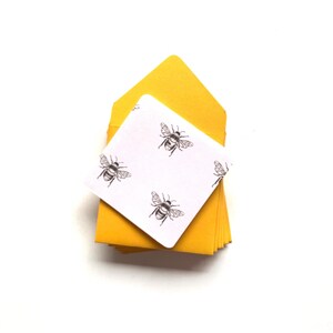May include: A stack of yellow envelopes with a white card on top. The card has a repeating pattern of black bees.