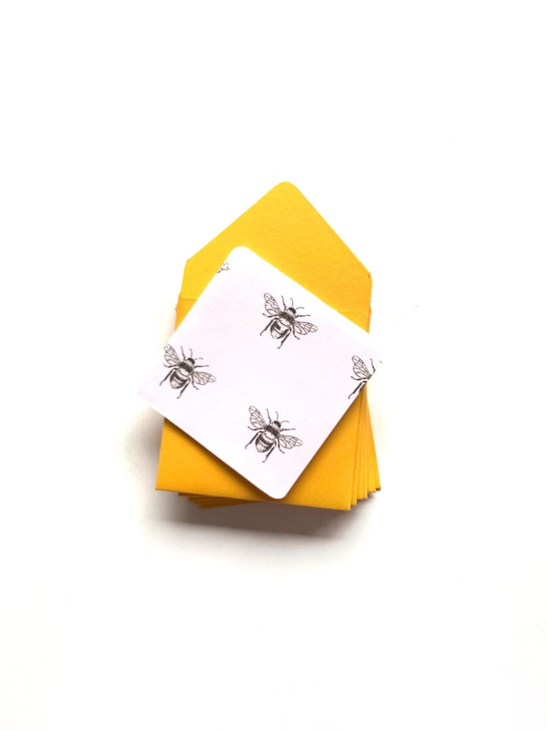 May include: A stack of yellow envelopes with a white card on top. The card has a repeating pattern of black bees.