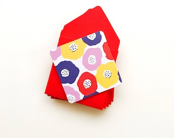 May include: A stack of red envelopes with a colorful floral patterned card on top. The card features a variety of flowers in shades of red, yellow, blue, and pink.