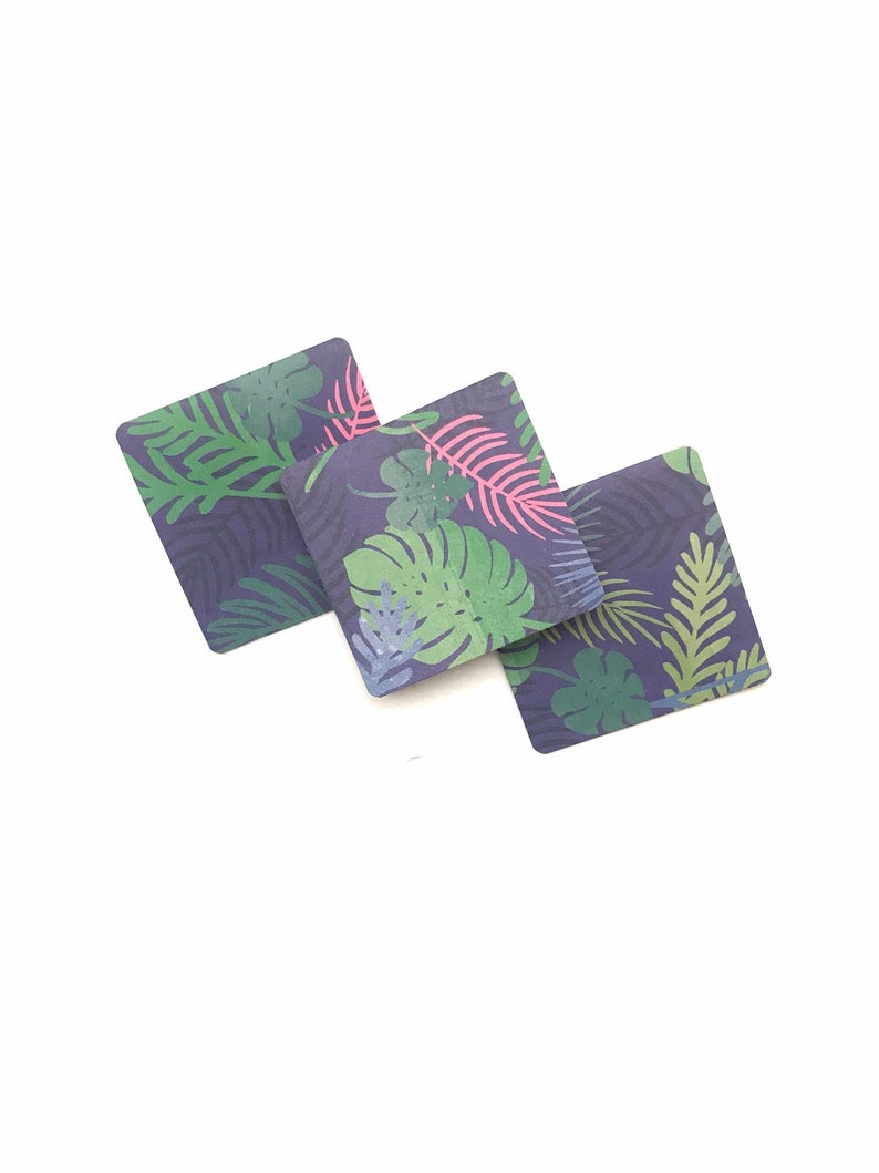 Puede incluir: Tres posavasos cuadrados con un patr&oacute;n de hojas tropicales. Los posavasos son de color azul oscuro con hojas verdes, rosas y azul claro.