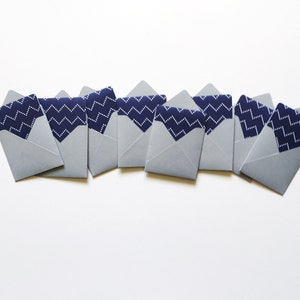 May include: A row of eight small, gray envelopes with a navy blue and white chevron pattern on the inside flap.