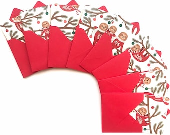 Op de afbeelding: Een set van tien rode enveloppen met witte papieren inlegvellen met een feestelijk luiaardontwerp. De luiaards dragen rode truien en houden kerstversiering vast. De enveloppen zijn perfect om kerstgroeten te sturen.
