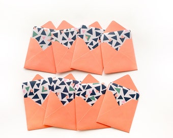 May include: Eight small, peach-colored envelopes with a geometric pattern of black, green, pink, and white triangles on the inside.