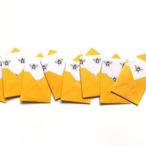 May include: A row of yellow envelopes with white paper inside, each decorated with a black and white bee pattern.